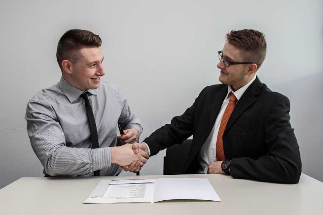 Two men facing each other while shake hands and smiling