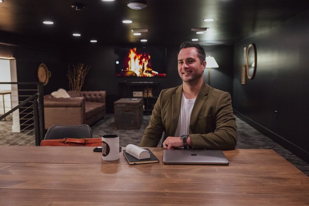 Man sits at a desk with a fireplace in background.