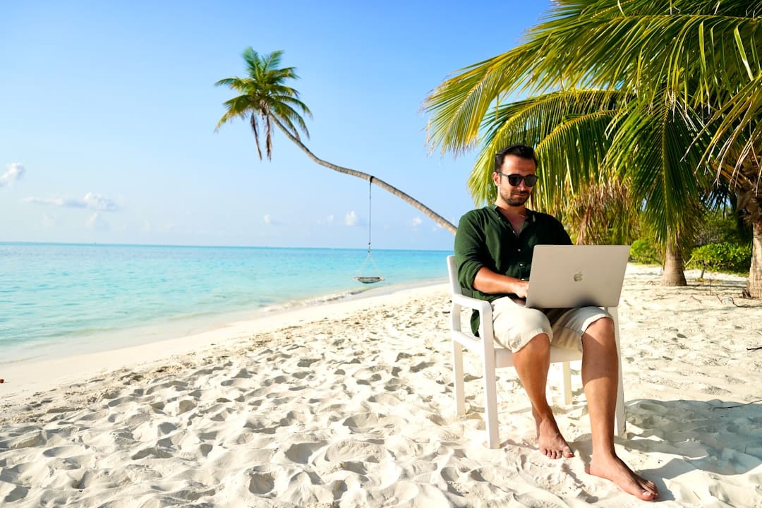 A man sitting in a chair on a beach using a laptop